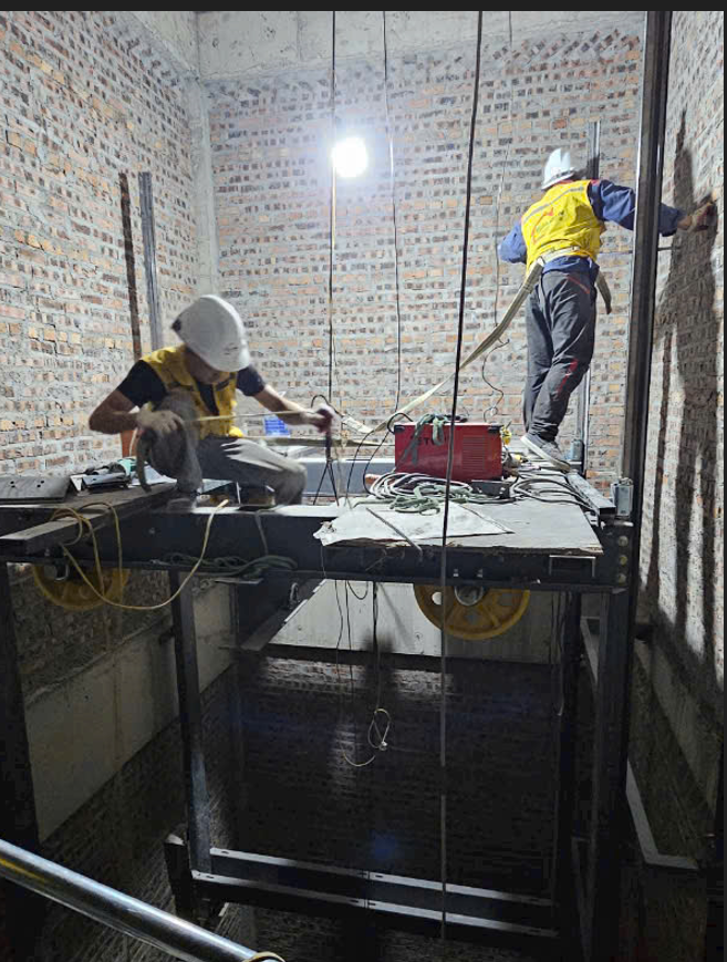 Kỹ thuật viên lắp đặt thang máy trong giếng thang đang thi công hệ thống cơ khí và điện